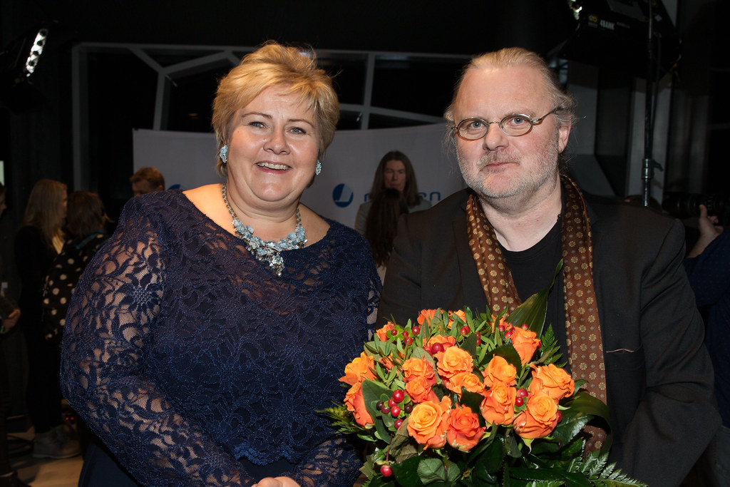 Den norske 2023 års vinnare av Nobelpriset i litteratur - Jon Fosse - tillsammans med Norges dåvarande statsminister Erna Solberg, i samband med Fosse vann Nordisk rådets Litteraturpris 2015. Erna Solberg står vänster i bild en blå festklänning och Jon Fosse till höger med en bukett orange blommor i handen.